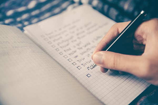 A close up of a hand writing a to-do list in a note book.