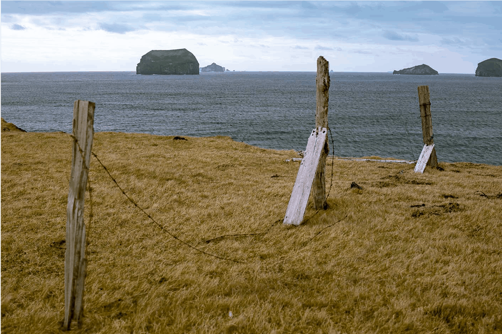 A broken, driftwood fence at the bottom of a cliff face with an ominous looking sky and sea in the background.